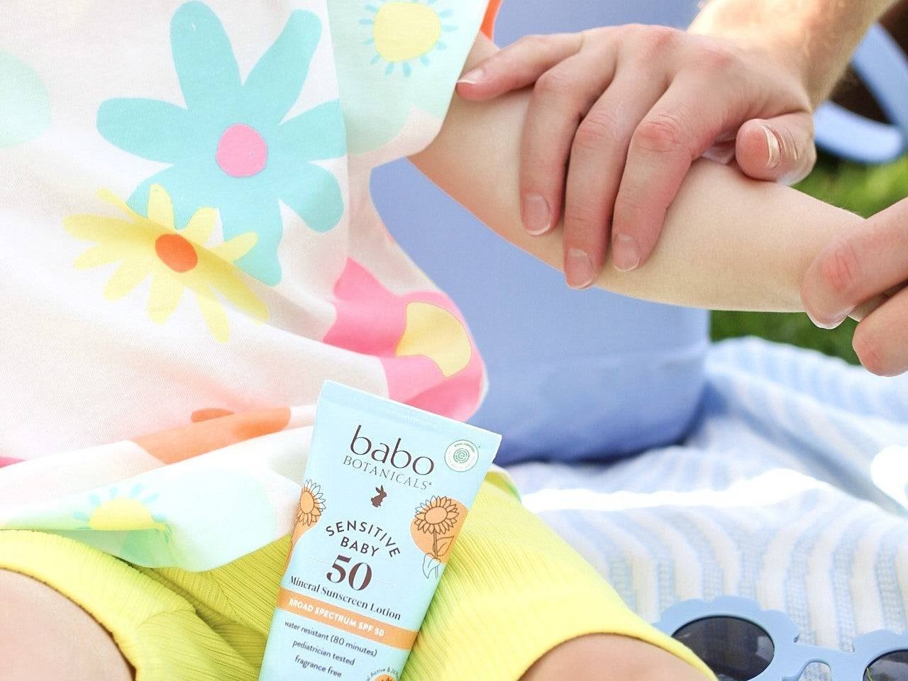 An adult rubs lotion onto a child during outdoor sun protection.