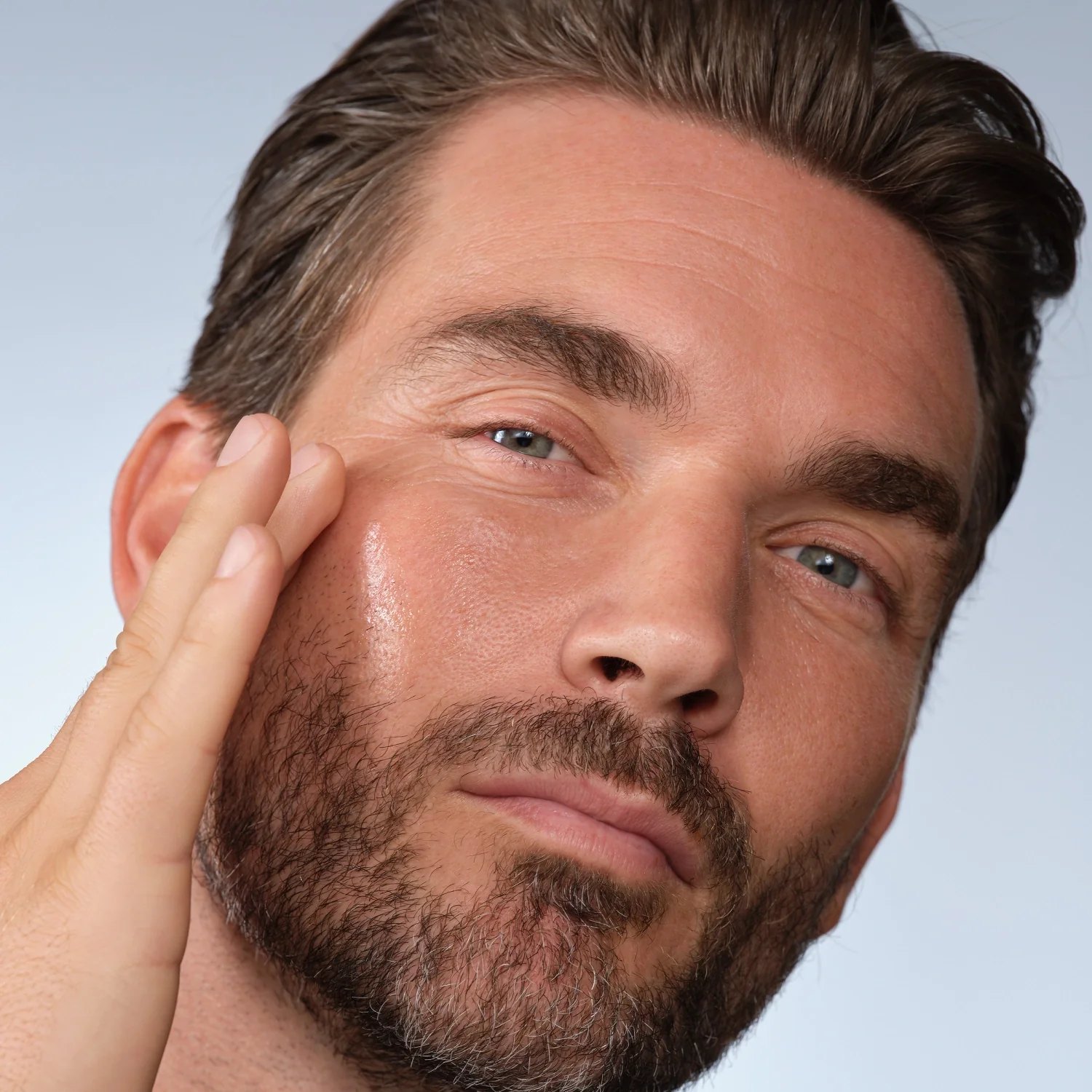 A man applies skincare to his cheek with his fingertips.