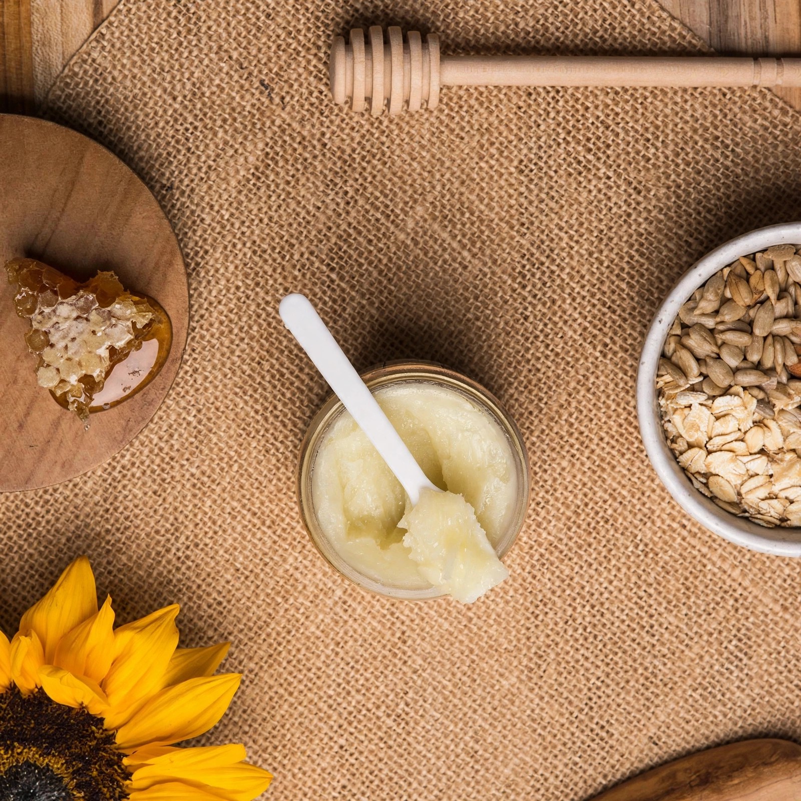 Natural honey and oatmeal ingredients styled with sunflower on fabric.