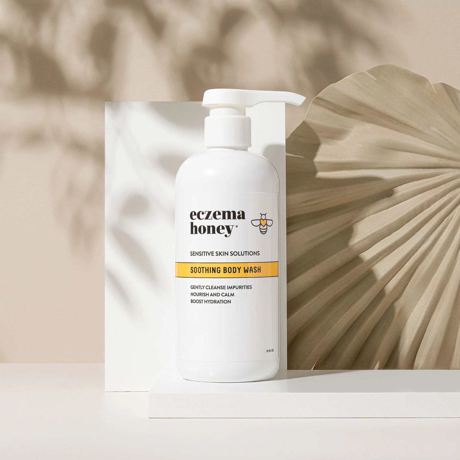 Eczema Honey body wash beside white block and palm leaf.