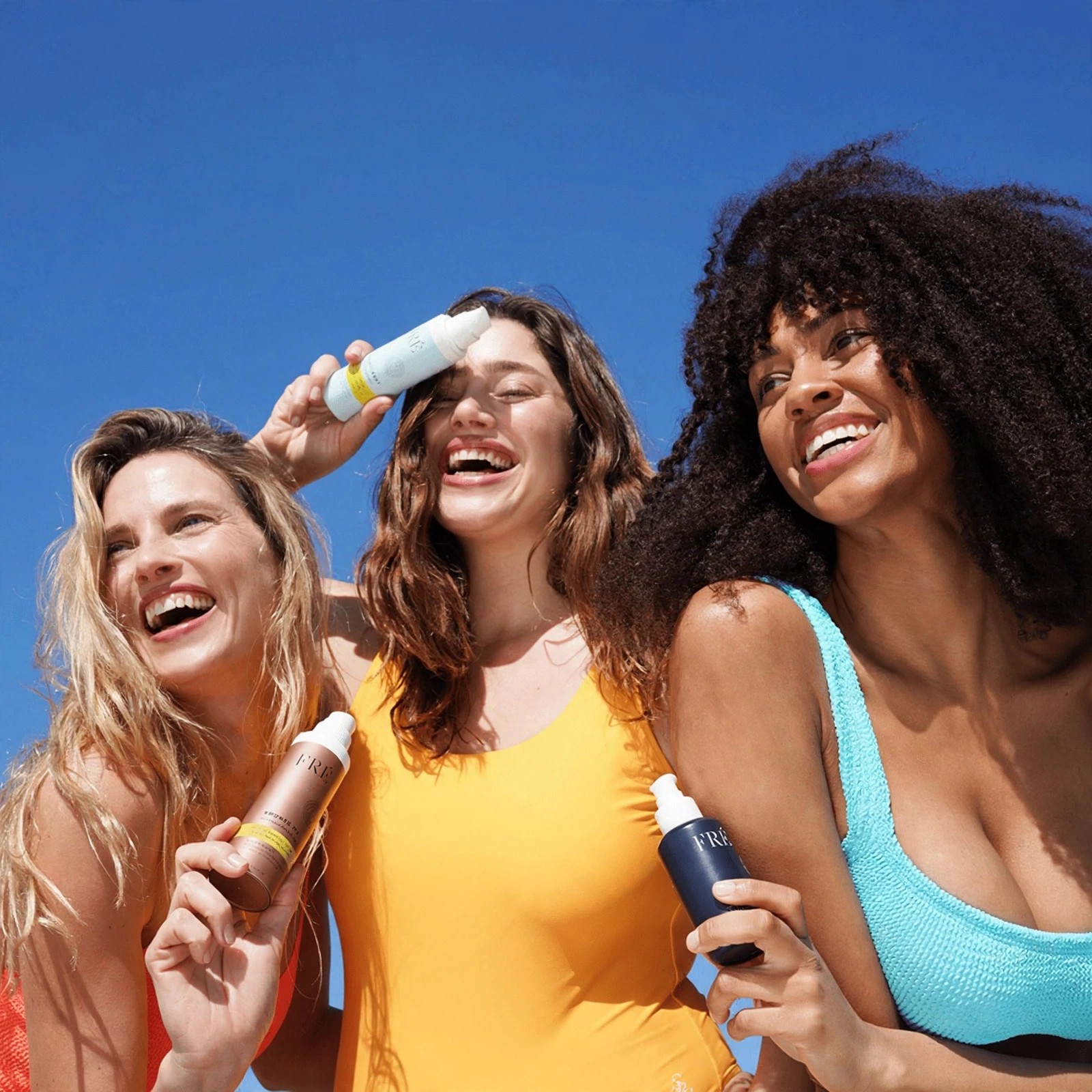 Friends in swimwear posing together with skincare bottles.