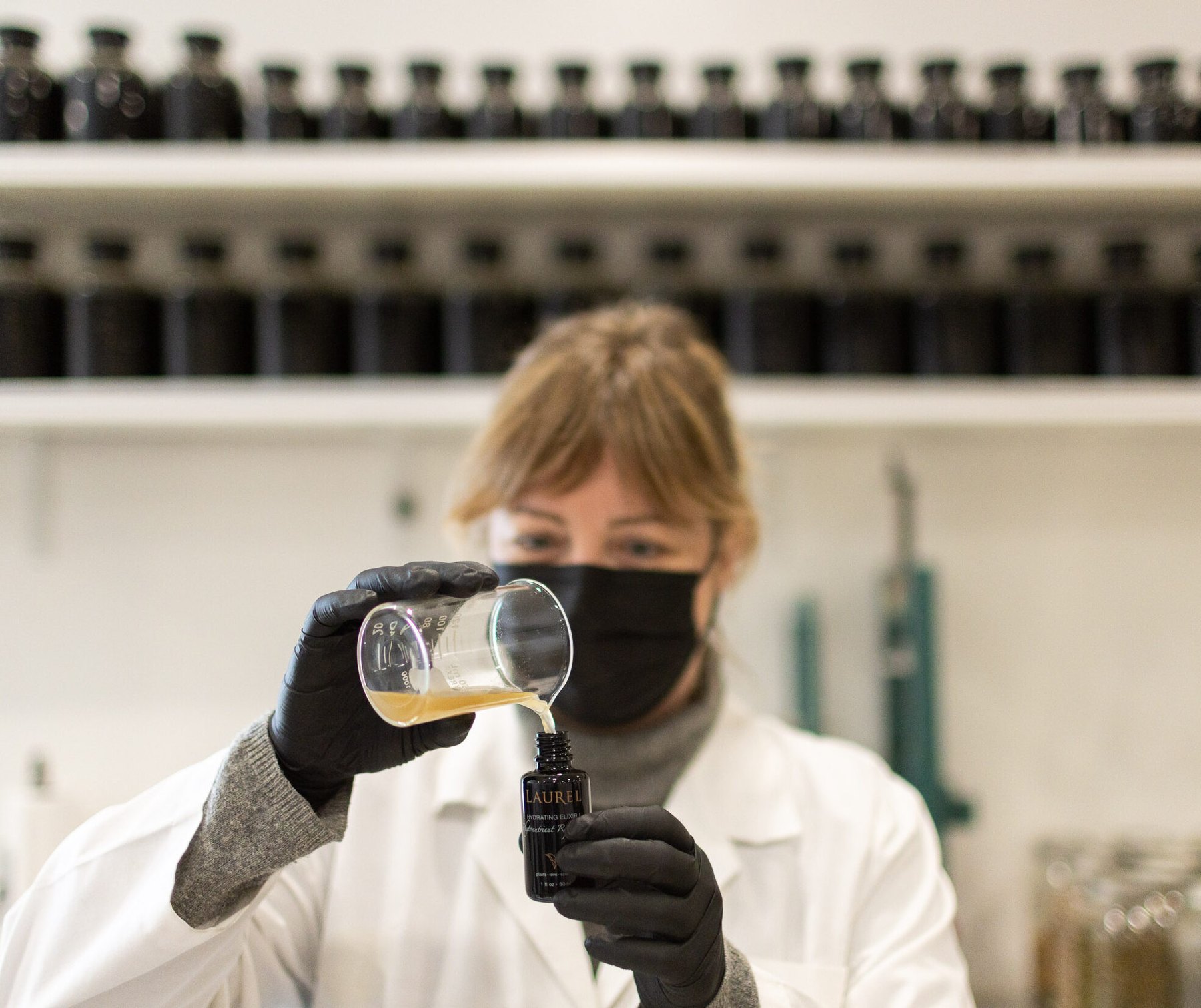A worker in a lab coat pours extract into a bottle.