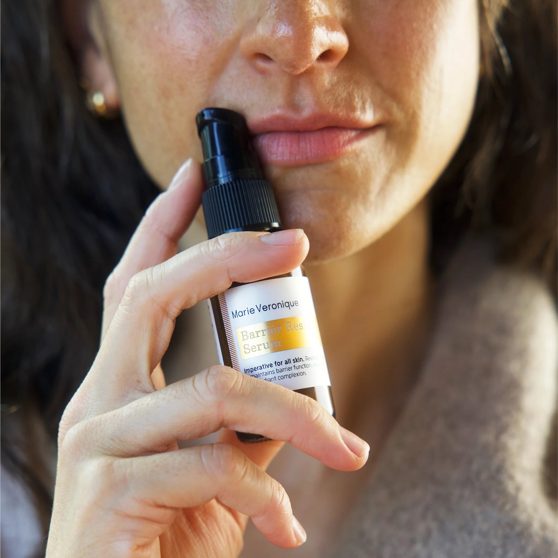 Hands present the Barrier Restore Serum bottle by a face.