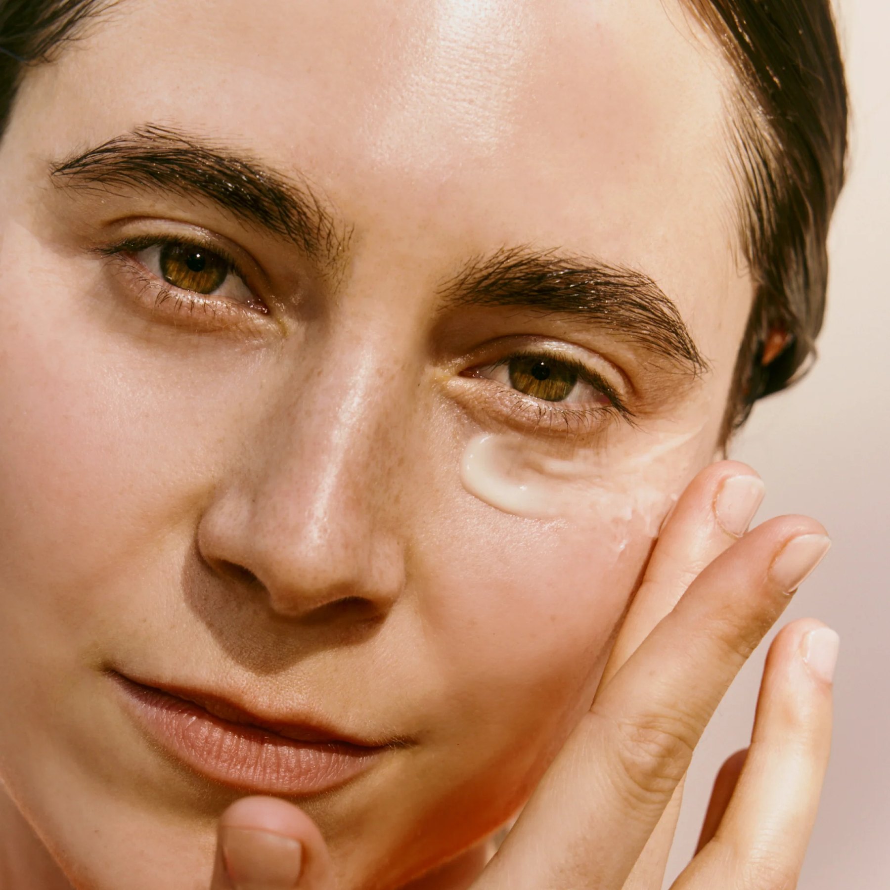 Close view of woman applying cream under one eye.