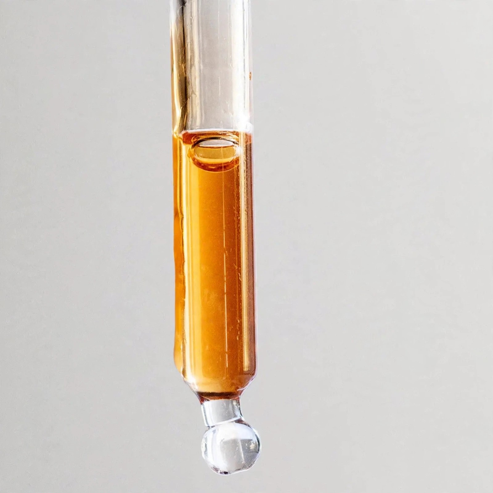 Close view of amber oil beading at a dropper tip.