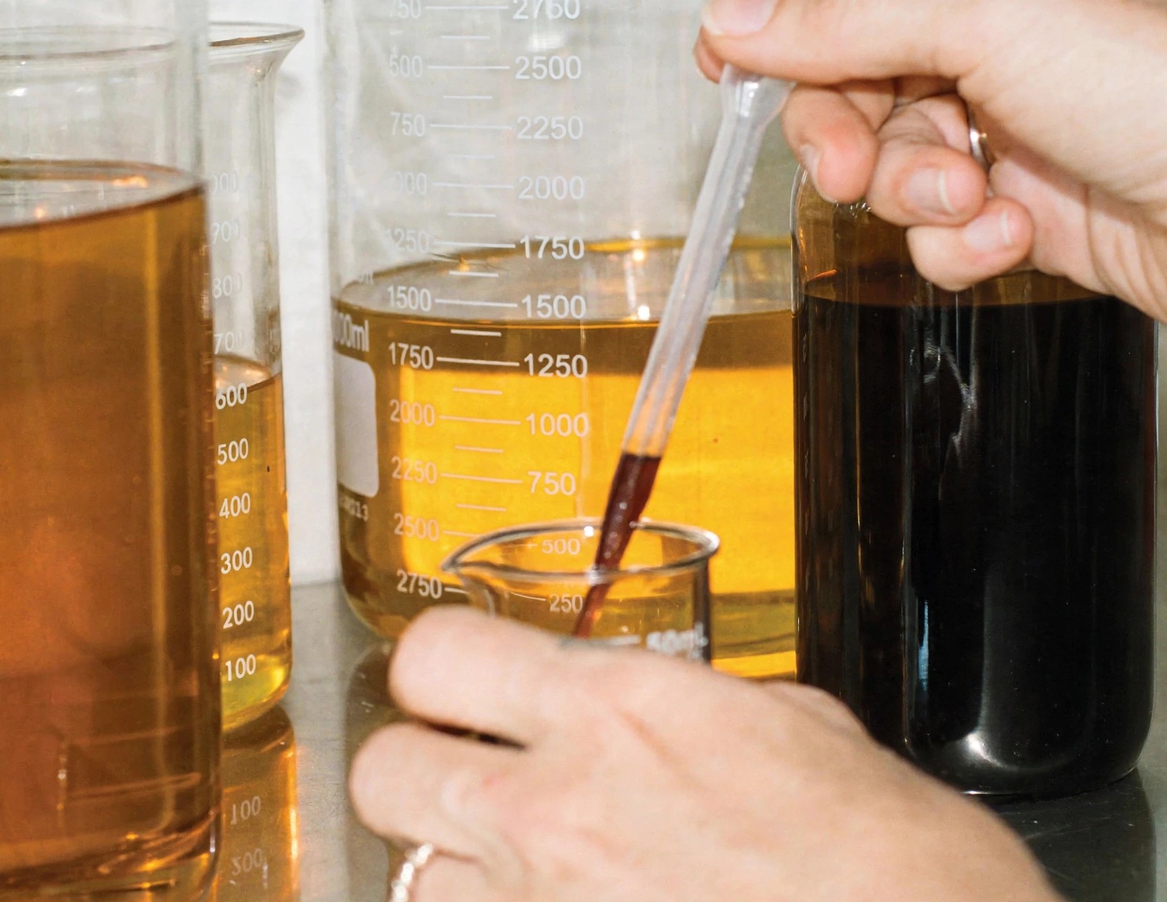 Close view of hands mixing oils in laboratory glassware.