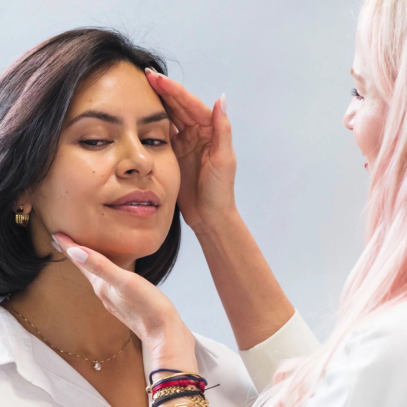 An esthetician examines a clients skin with hands on face.