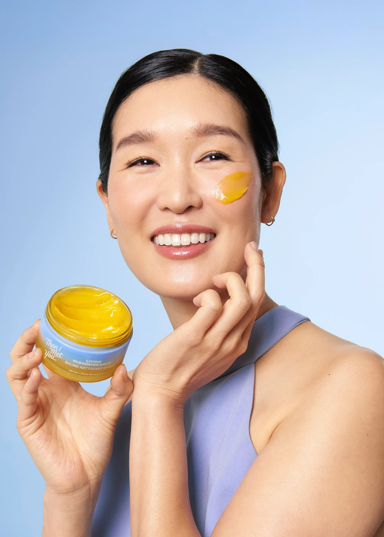 Model displays cleansing balm jar and textured cheek swatch.