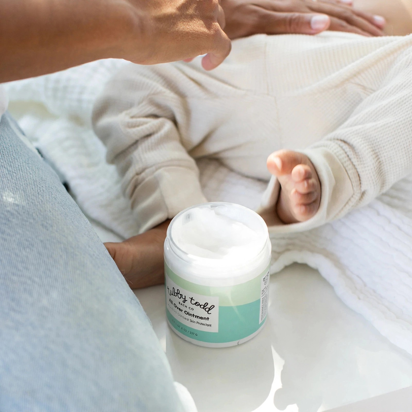 Baby feet near an open Tubby Todd ointment jar.
