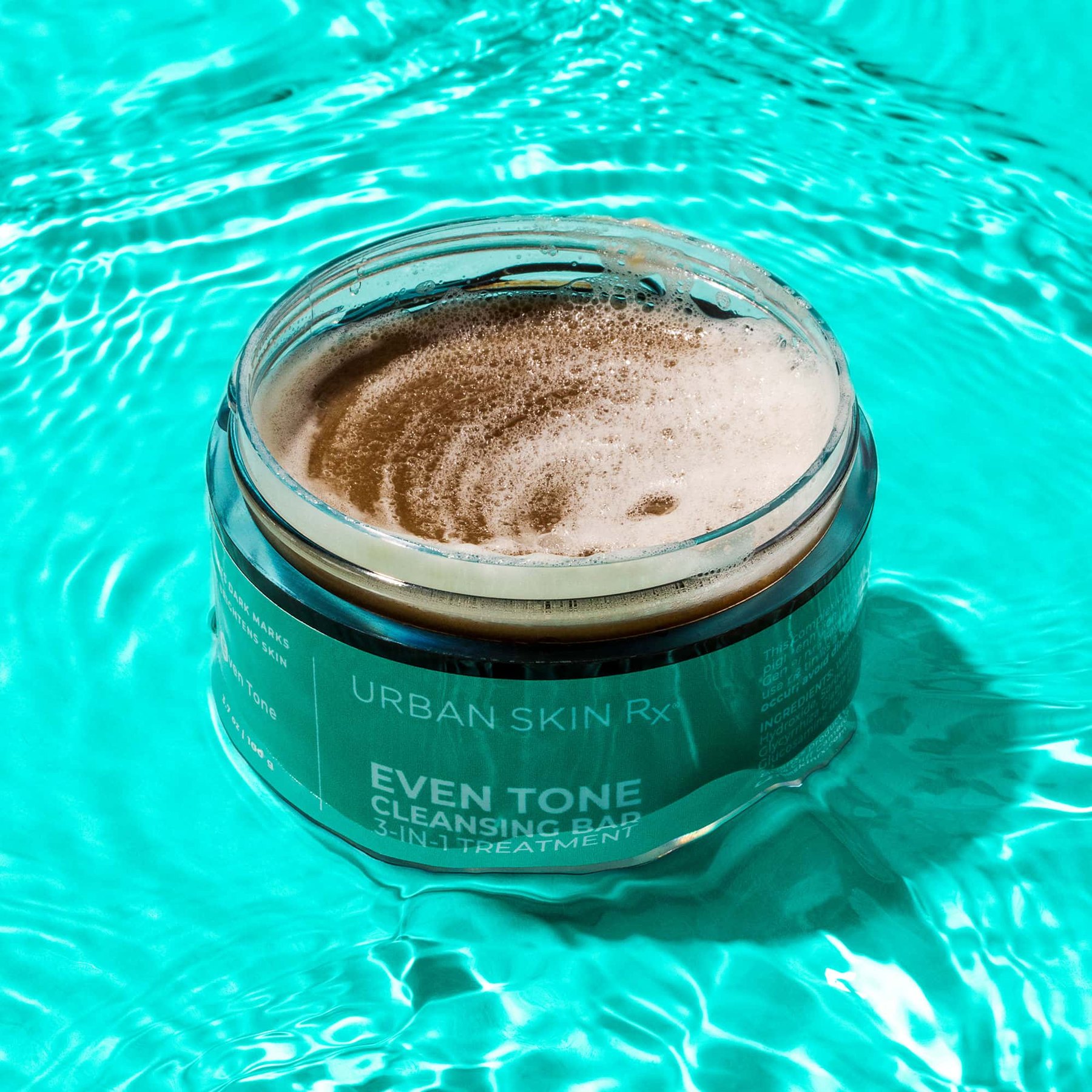 Lathering cleansing bar in its jar floating in bright turquoise water.