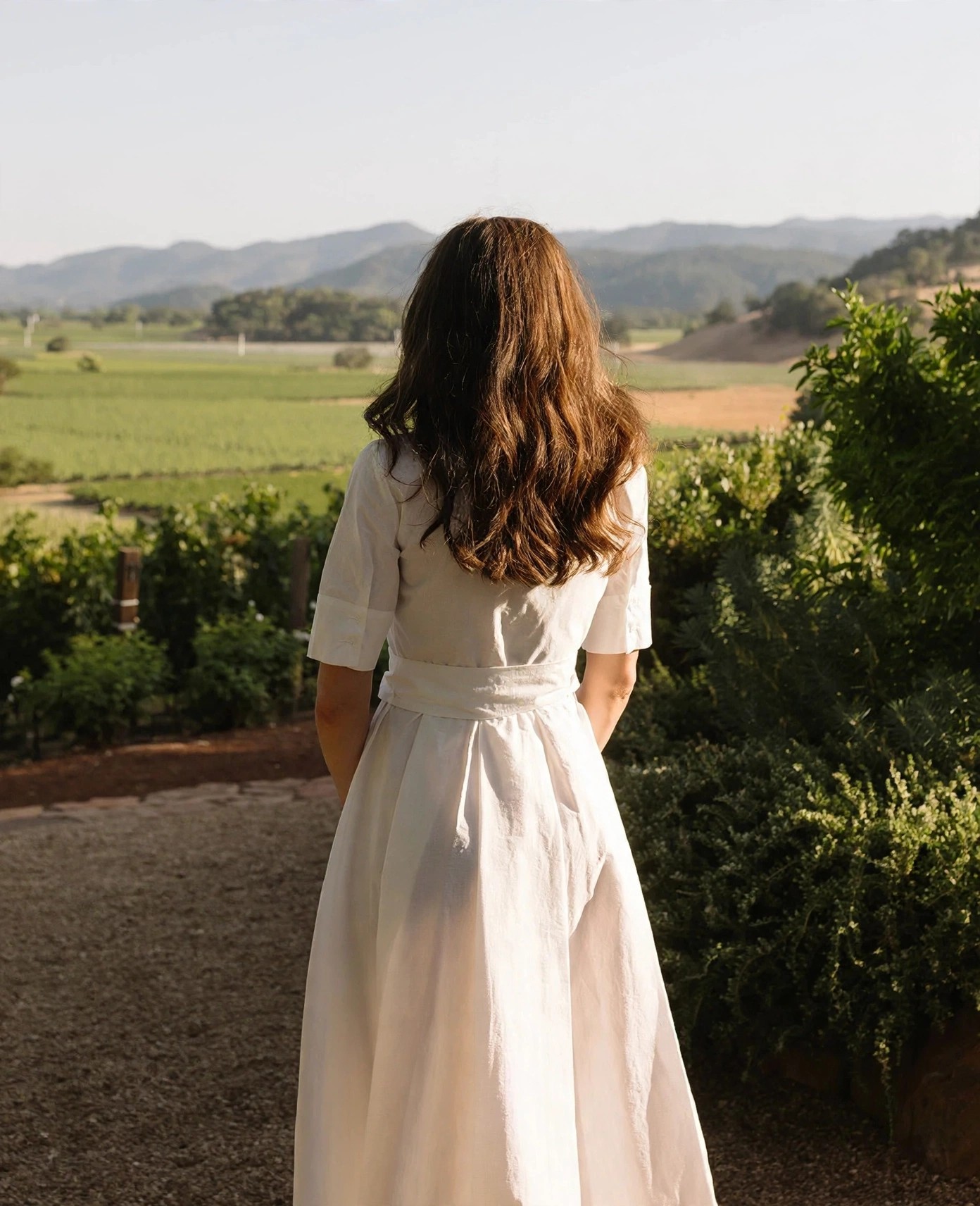 Rear view of woman overlooking green valley vineyards.
